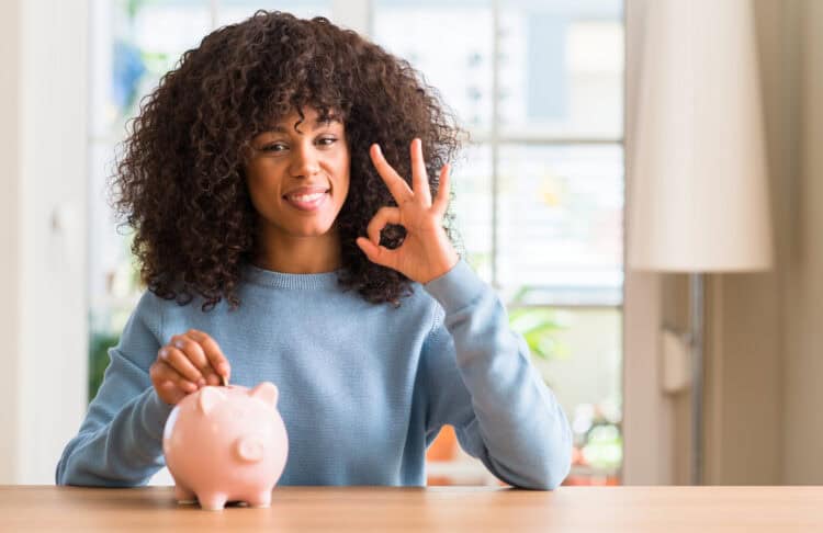 Woman saves money in piggy bank doing ok sign with fingers, excellent symbol