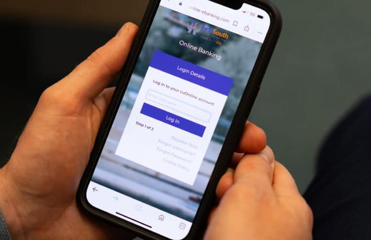 Hands holding a smartphone displaying online banking login screen, with a blurred background emphasizing the focus on mobile app interaction.